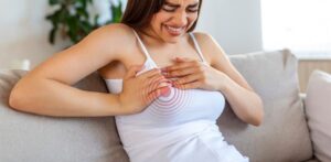 Woman on a sofa holding her breast in discomfort