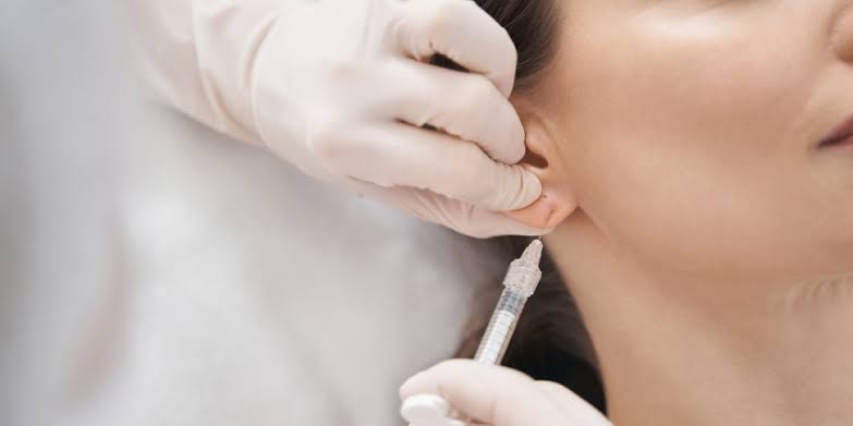 Gloved hands giving a local anaesthetic injection near the earlobe